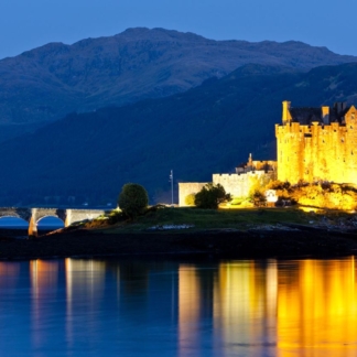 Eilean Donan Castle illuminated at night, reflecting on Loch Duich in Scotland